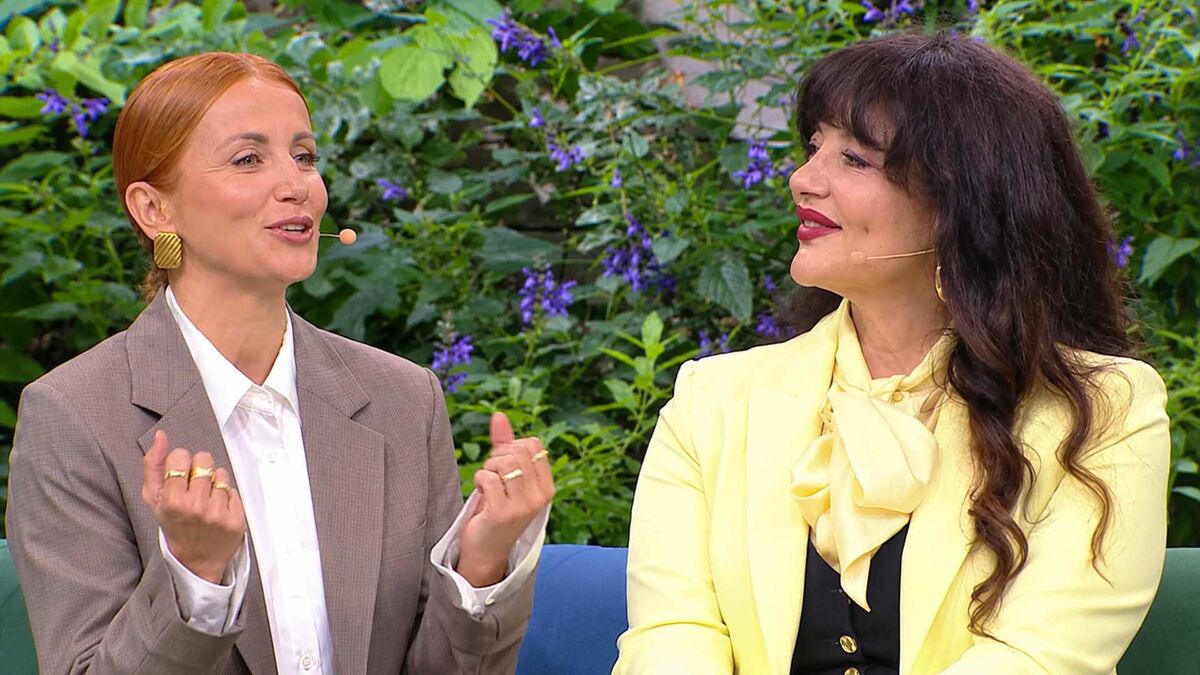 Katarzyna Zielińska siedzi obok uczestniczki programu „Europa da się lubić. Nowe Pokolenie” i gestykuluje dłońmi podczas rozmowy. Obie kobiety mają przypięte mikrofony, a uczestniczka jest ubrana w jasnożółty garnitur z wiązaną bluzką. Za nimi znajduje się gęsta zielona roślinność z fioletowymi kwiatami.